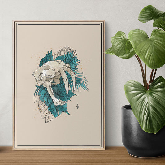 Photo of art print framed sitting on wooden table, plant on the right. Bold design of big sabertooth skull with loads of teal tropical forest leaves. Light cream background and tiny rune. 